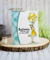 The girl and her balloons colored in soft yellow on a teal-plaid card staged on a wood slice.