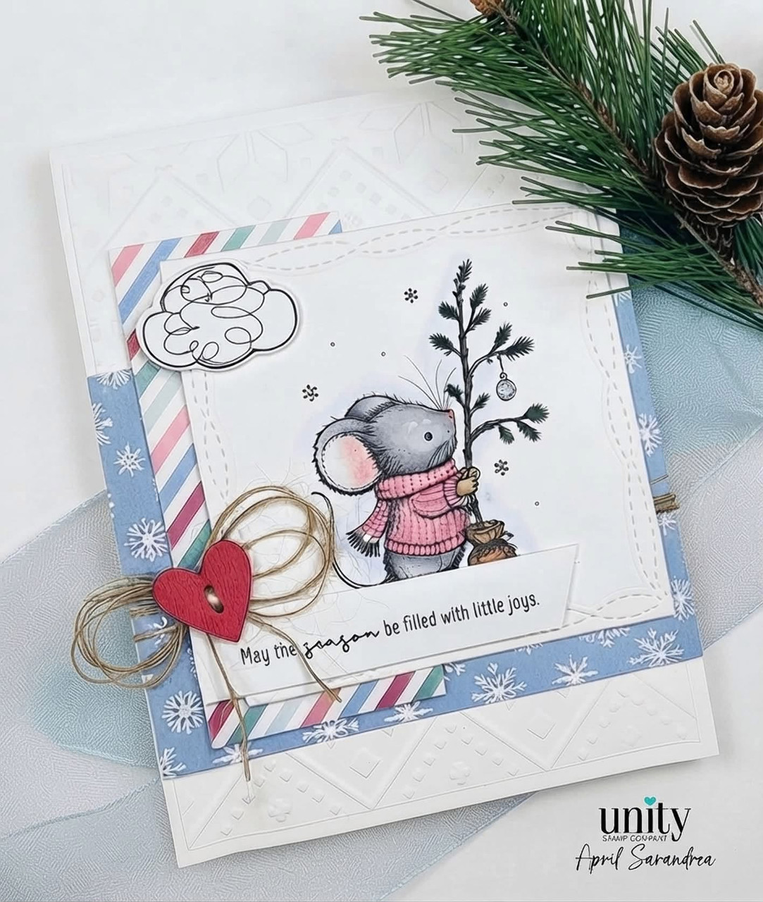 A blue and white card with the mouse in a pink sweater standing beside a small decorated tree under a stamped cloud, above a strip reading 'May the season be filled with little joys.'
