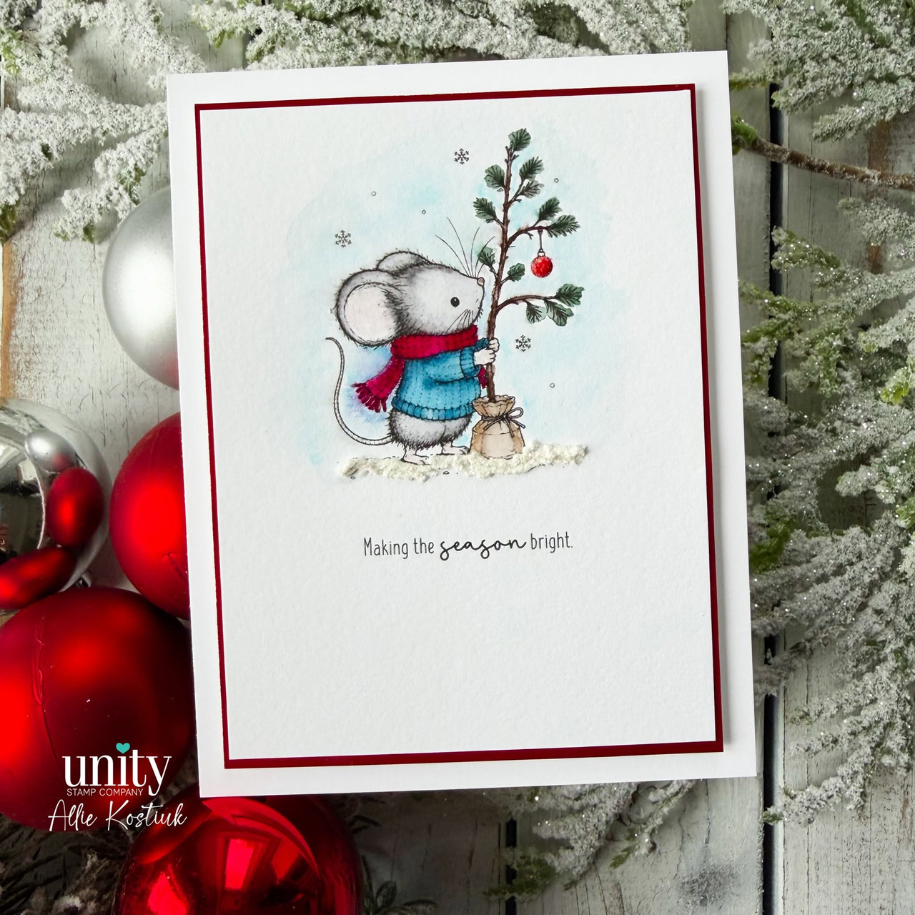A deep red framed card with the mouse in a blue scarf beside a small tree, watercolored on a pale blue sky with snow at the base, above 'Making the season bright.'