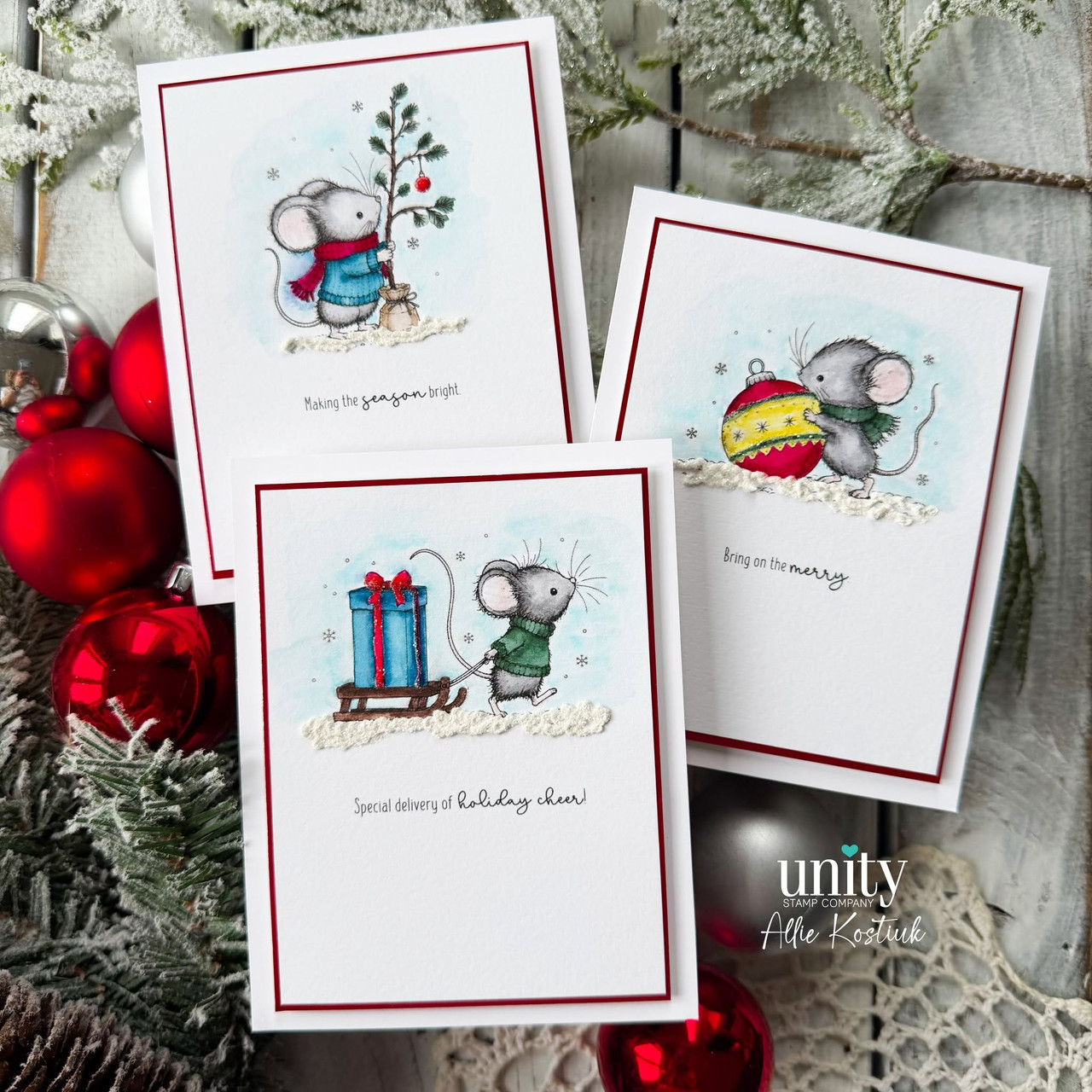 Three finished mouse cards fanned out together among red and silver ornaments, each watercolored with its own sentiment strip.
