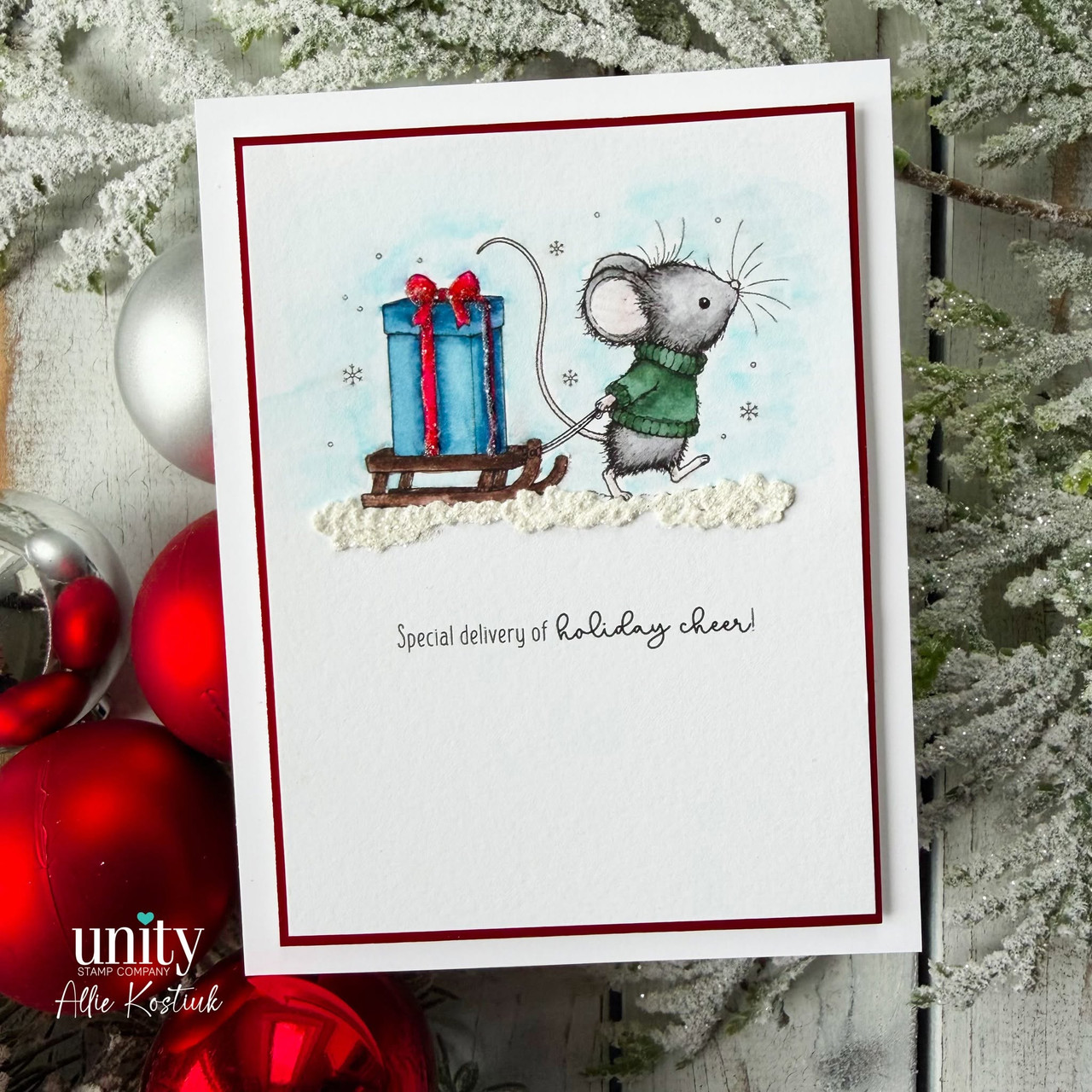 A deep red framed card with the mouse in a green sweater hauling a blue gift on a wooden sled through the snow, above 'Special delivery of holiday cheer!'