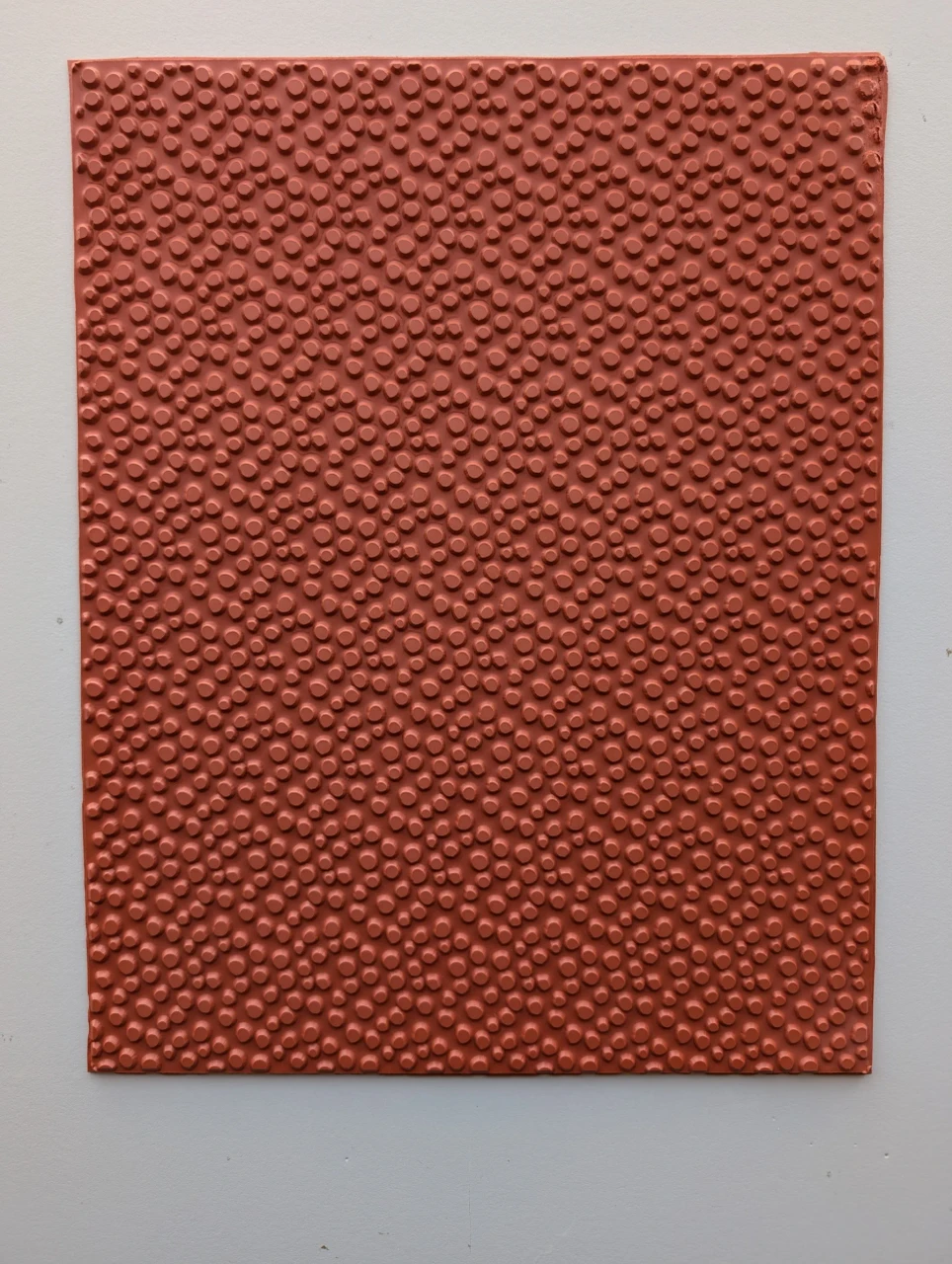 Full sheet of red vulcanized rubber covered with irregular raised pebble shapes in mixed sizes.