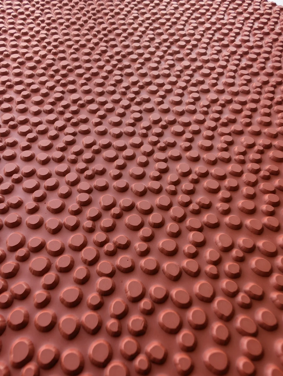 Close view of mixed-size raised pebble shapes on a flexible red rubber pottery texture mat.