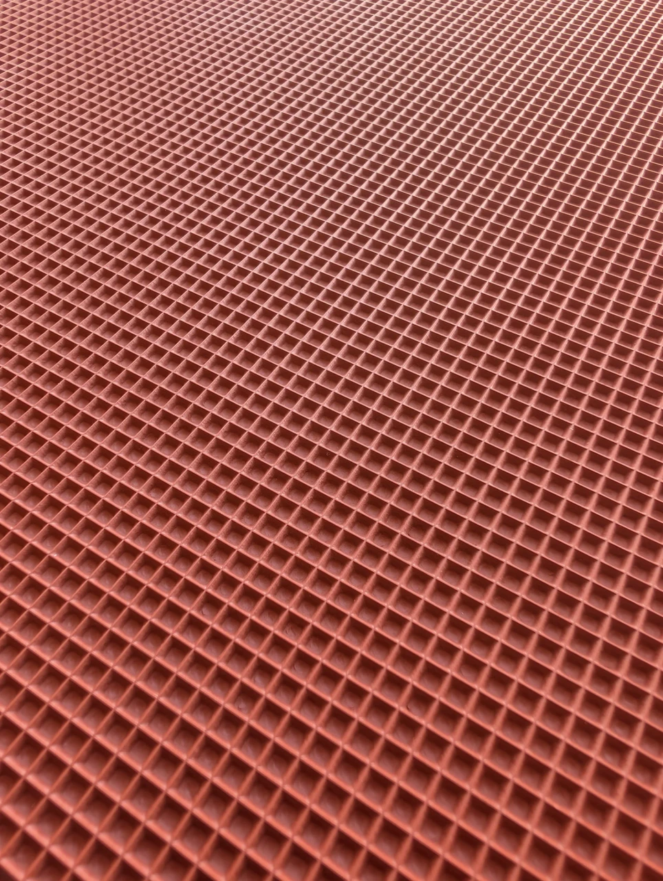 Close view across the fine square grid on a red vulcanized rubber texture mat.