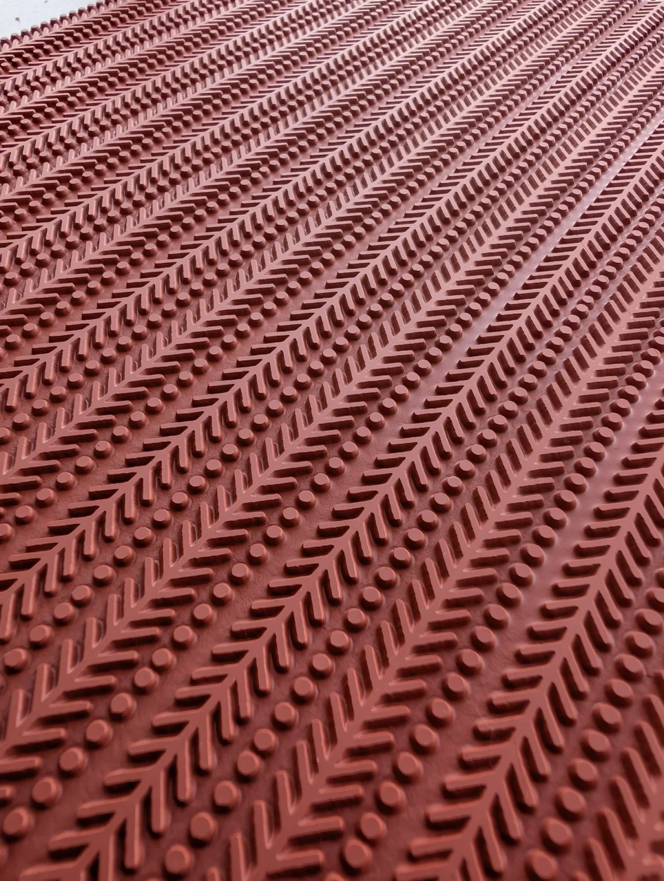 Angled close view of raised herringbone lines and dots on a red rubber texture mat.