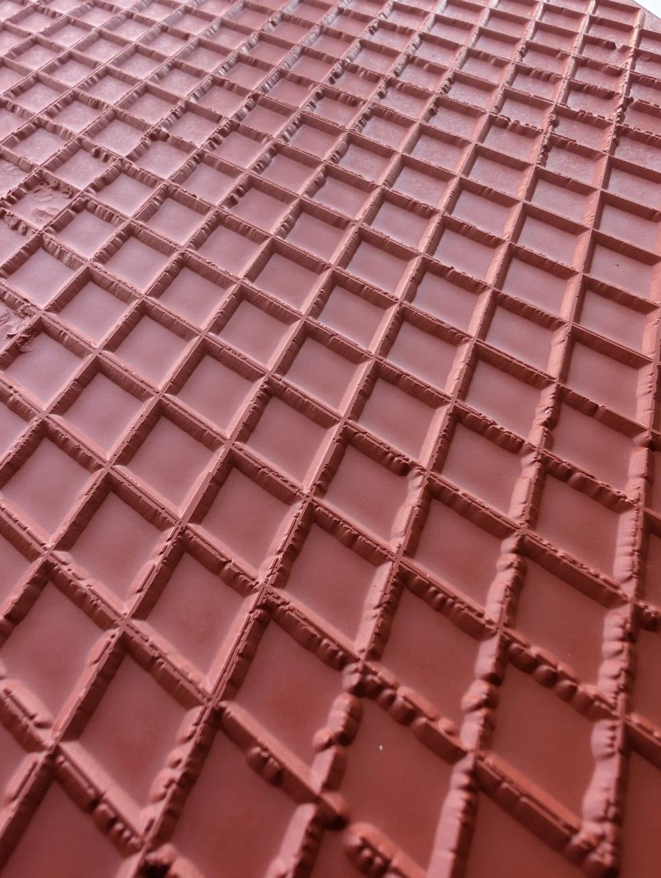 Close view across the raised diamond lattice pattern on a red rubber texture mat.