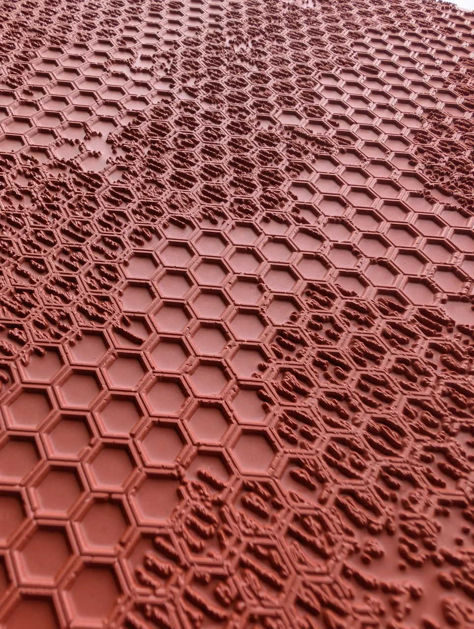 Close view of raised hexagon outlines merging with rough broken texture on a red rubber pottery mat.