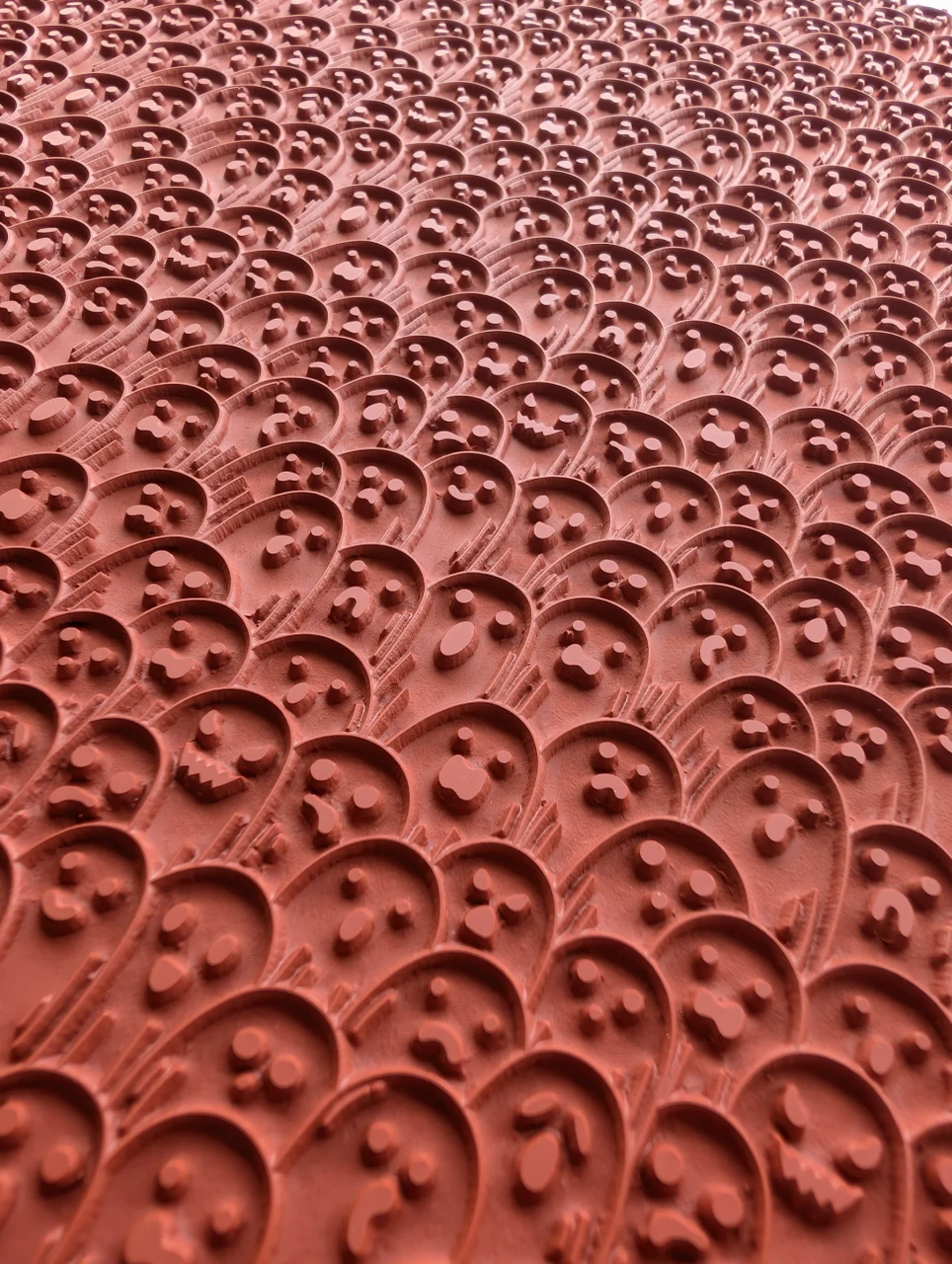 Close view across raised ghost faces with varied eyes and mouths on a red rubber pottery texture mat.