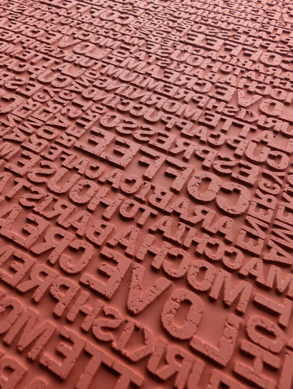 Close view of overlapping raised uppercase letters with distressed faces on a red rubber pottery texture mat.