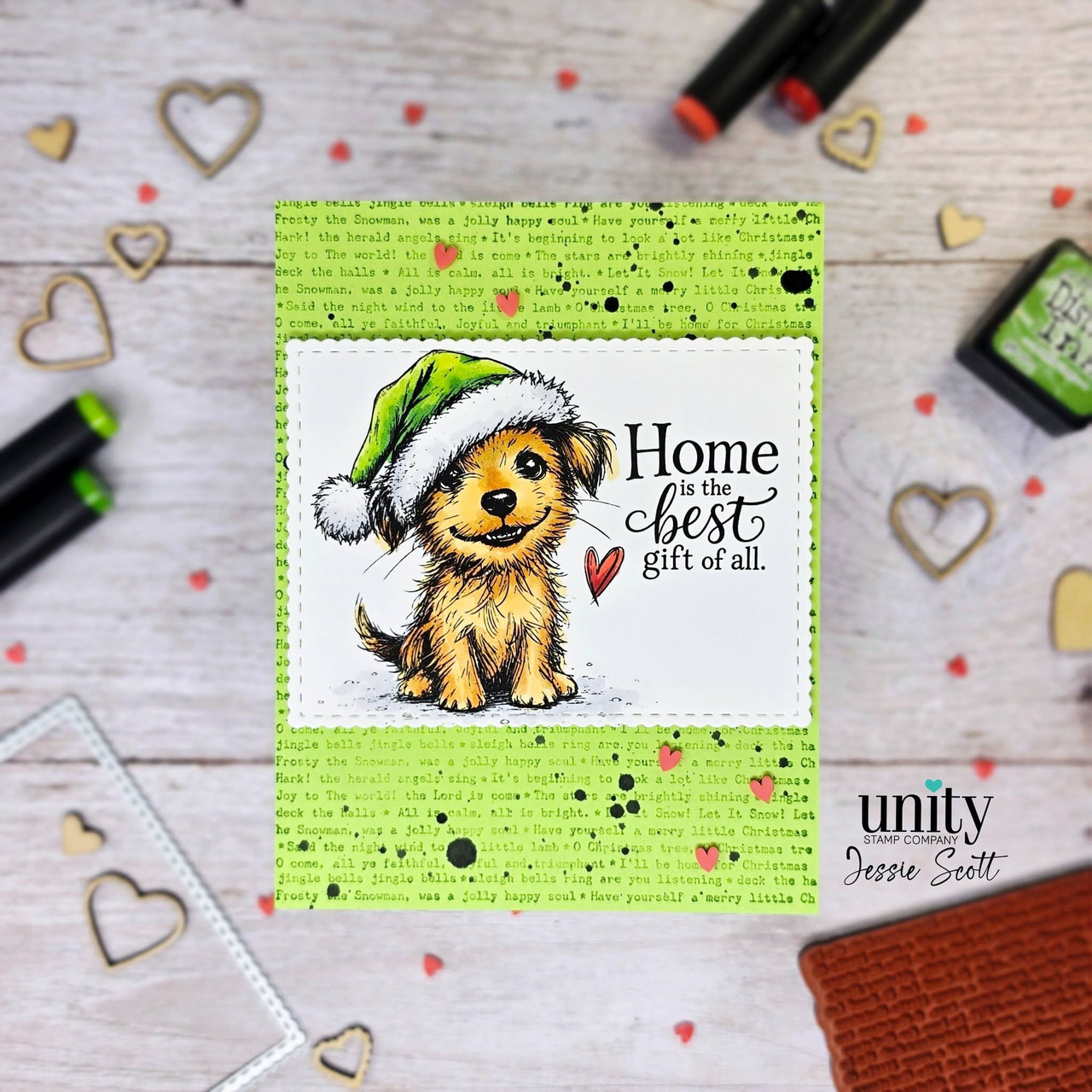 Card with Odie the puppy colored golden in a lime green Santa hat with a red heart, 'Home is the best gift of all.' beside him, on a bright green text background with black ink splatters.