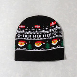 A black knitted beanie featuring festive designs, including smiling Santa faces and snowflakes. It has a logo.