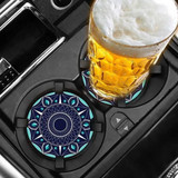 A drink coaster featuring a vibrant blue and turquoise mandala design, placed in a car cup holder alongside a glass of beer.