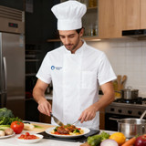 A chef in a white double-breasted chef jacket and hat prepares a gourmet dish in a modern kitchen.