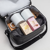 A cooler bag in dark grey containing two white mugs, a box of drinking chocolate, and a box of marshmallows.
