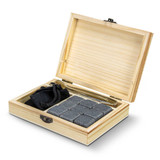 A wooden gift box containing grey whiskey stones, a black pouch, and a stainless steel tongs.