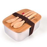 A silver lunch box with a wooden lid, featuring bamboo utensils and secured with a brown strap.