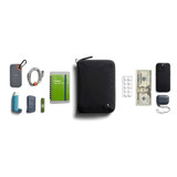 A black toiletry bag with various items including a drink bottle, notebook, cash, and an inhaler. It has a logo.