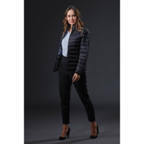 A woman in a black puffer jacket poses against a dark background, wearing tailored black trousers and high heels.