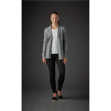 A woman wearing a grey Women's Soho Cardigan over a white top, paired with black leggings. The background is dark.
