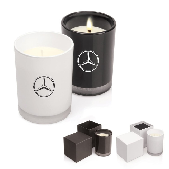 A set of two scented candles in white and black glass containers, both featuring a logo.