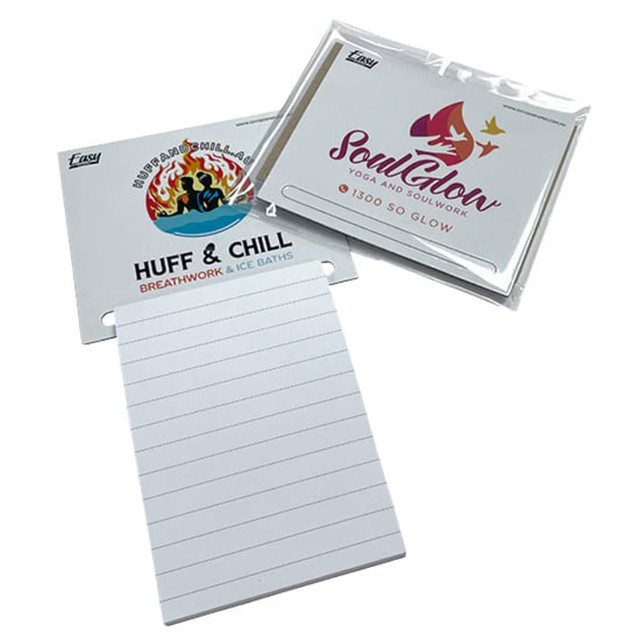 A magnetic shopping list notepad in white with line sections, accompanied by two branded card designs.