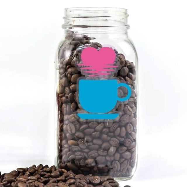 A clear glass jar filled with coffee beans, featuring a blue cup and pink heart sticker.