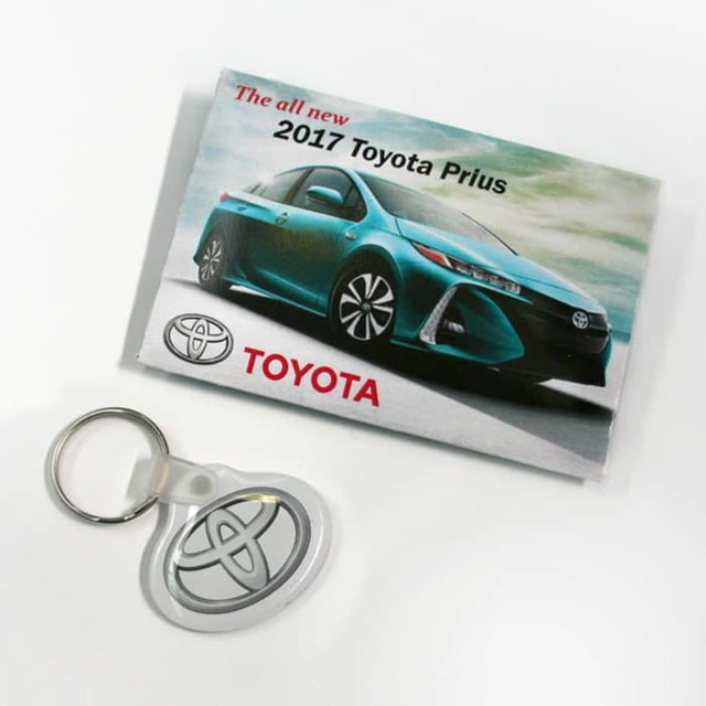 A promotional folder featuring a blue 2017 Toyota Prius and a silver key tag. The folder has a logo.