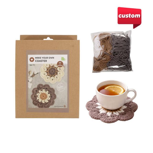 A crochet kit featuring yarn in brown, white, and grey, with a finished floral coaster design and a cup of tea.