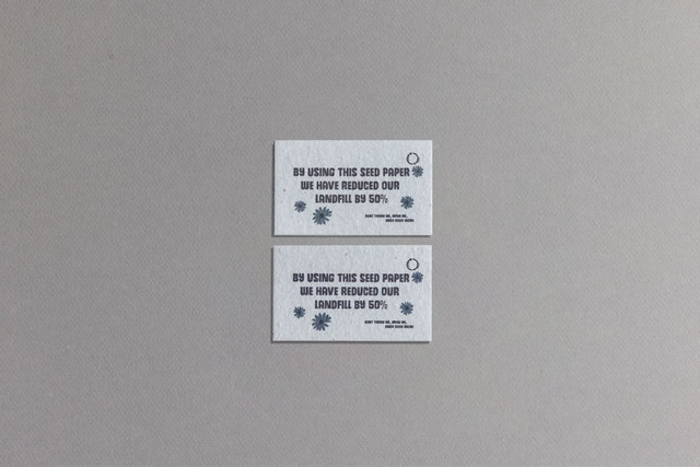 Two rectangular seed paper business cards in light grey with blue text and a circular logo, promoting sustainability.