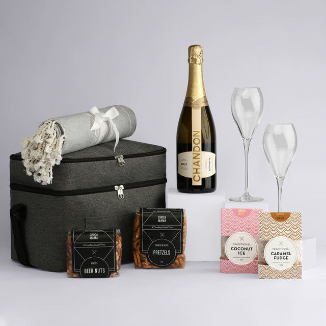A drink bottle with a grey blanket, two glasses, a bottle of sparkling wine, and assorted snacks in packaging.