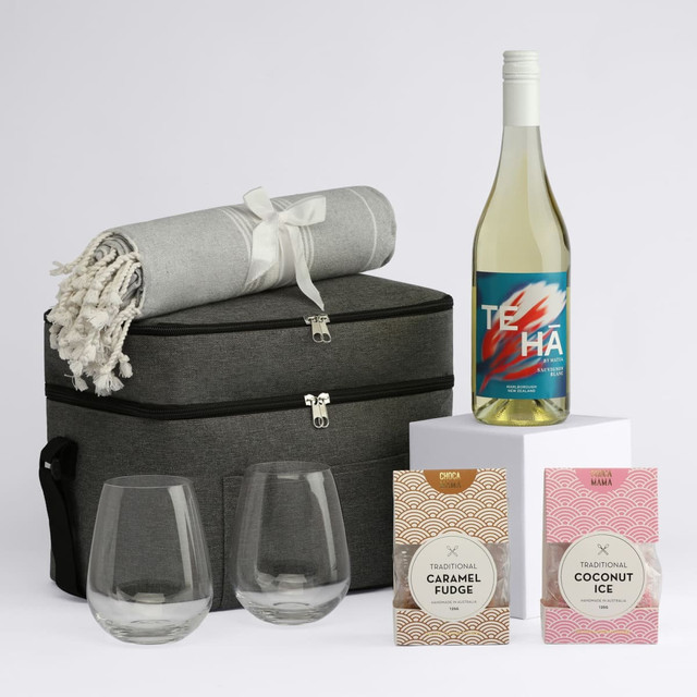 A drink bottle and two stemless glasses sit beside a picnic basket, blanket, and two gourmet treats in pink packaging.