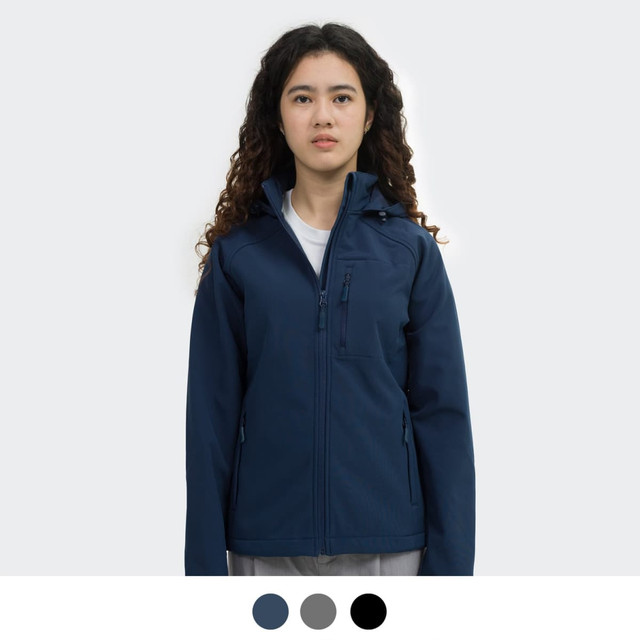 A woman is wearing a navy soft shell jacket with a hood, featuring a zip front and branding.