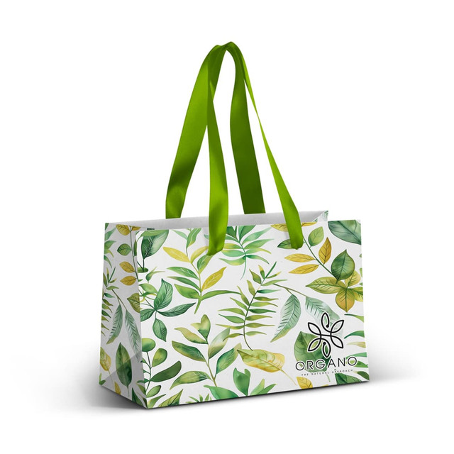 A small paper bag featuring a full-colour design of green leaves, with a green ribbon handle and a logo.