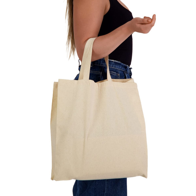 A beige reusable calico bag with short handles held by a person, featuring a simple design and no visible branding.
