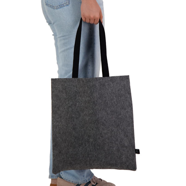 A grey felt tote bag with black handles is held by a person wearing jeans. The bag features a logo.
