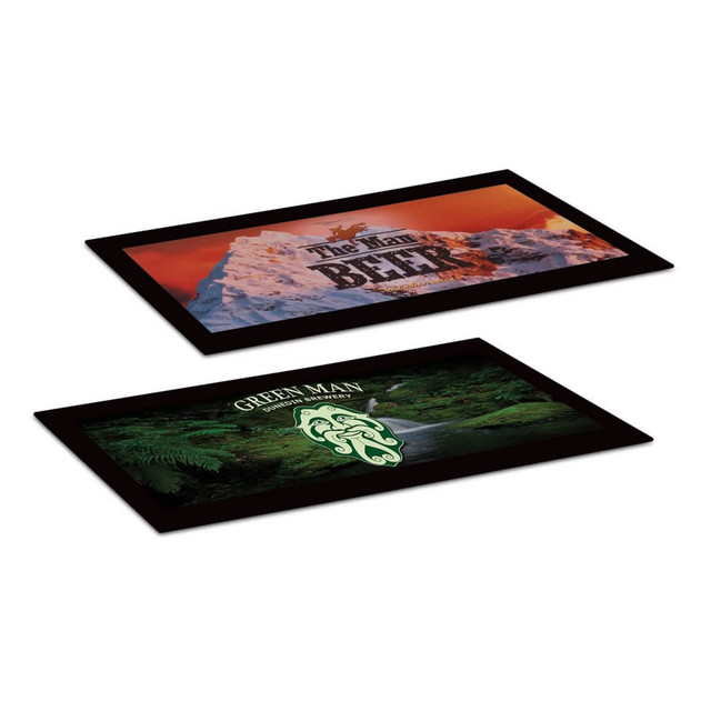 Two black counter mats featuring different designs: one with mountains and text, the other with a green logo and landscape.