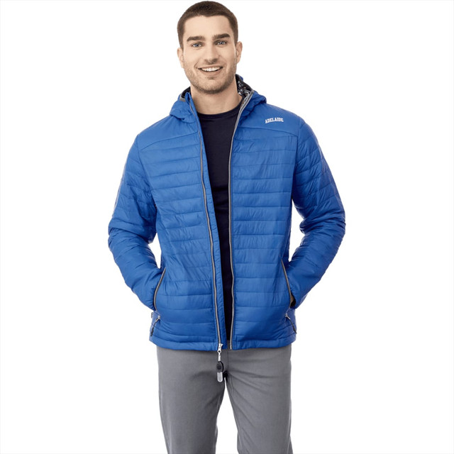 A man wearing a blue packable puffer jacket with a hood, featuring a logo. The jacket is zipped and has side pockets.