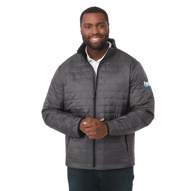 A man wearing a grey puffer jacket with a zip front and a logo on the sleeve.
