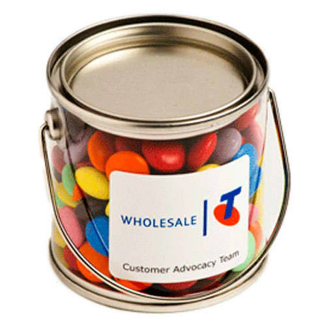 A small silver bucket filled with colourful chocolate beans, featuring a white label with a logo.