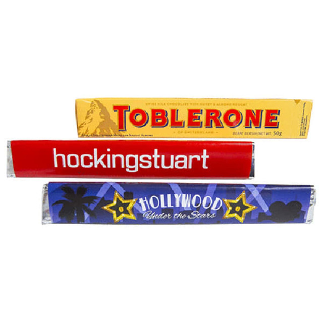 A Toblerone chocolate bar with a yellow sleeve, featuring red and blue wrapped items behind it.