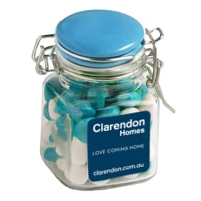A glass clip lock jar filled with chewy fruit sweets in blue and white, featuring a blue lid and a logo.