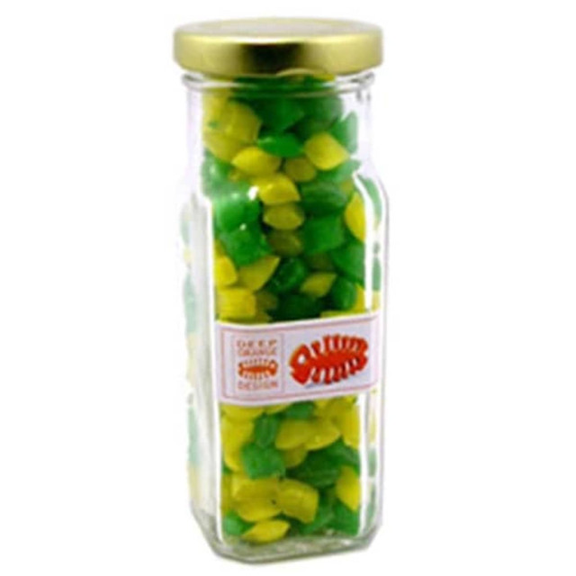 A tall glass jar with a gold lid, filled with green and yellow humbug sweets. The jar features a logo.