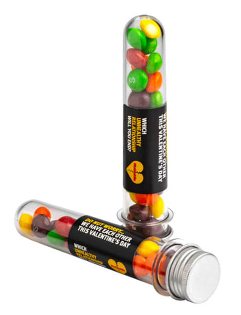 A clear test tube filled with colourful Skittles, featuring a silver cap and a branding label.