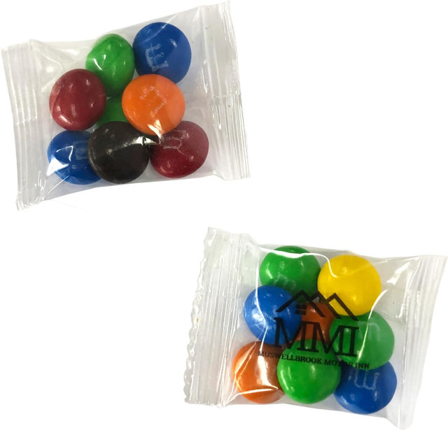 A plastic bag containing coloured chocolate candies, including blue, red, green, orange, yellow, and brown, with a logo.
