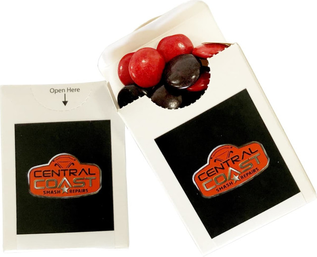 A flip lid cardboard box containing red and black choc beans, with a logo on the front.