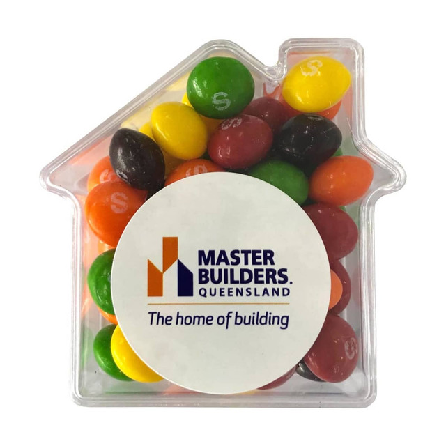 A clear acrylic house-shaped container filled with colourful Skittles in various shades. It features a logo on the front.