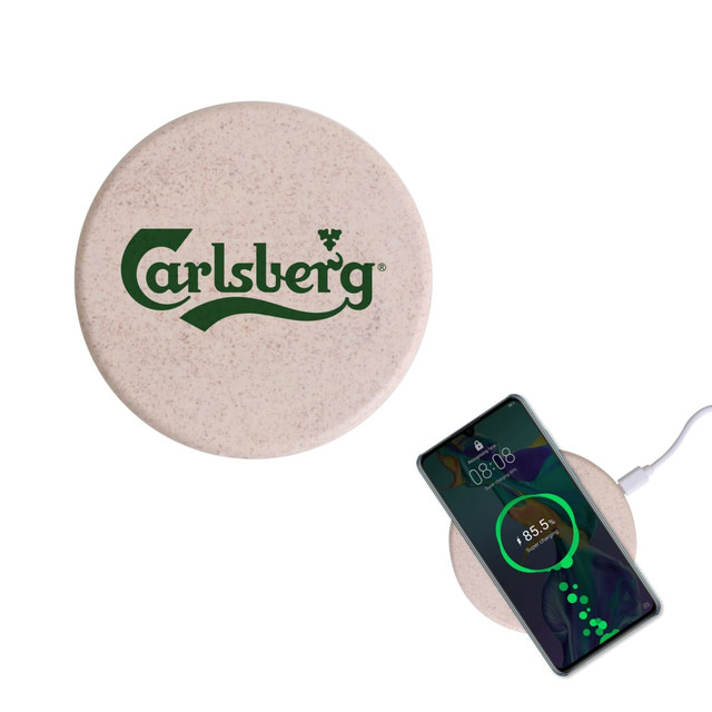 A round wheat straw wireless charger in a light beige colour with a logo, next to a smartphone displaying charging progress.