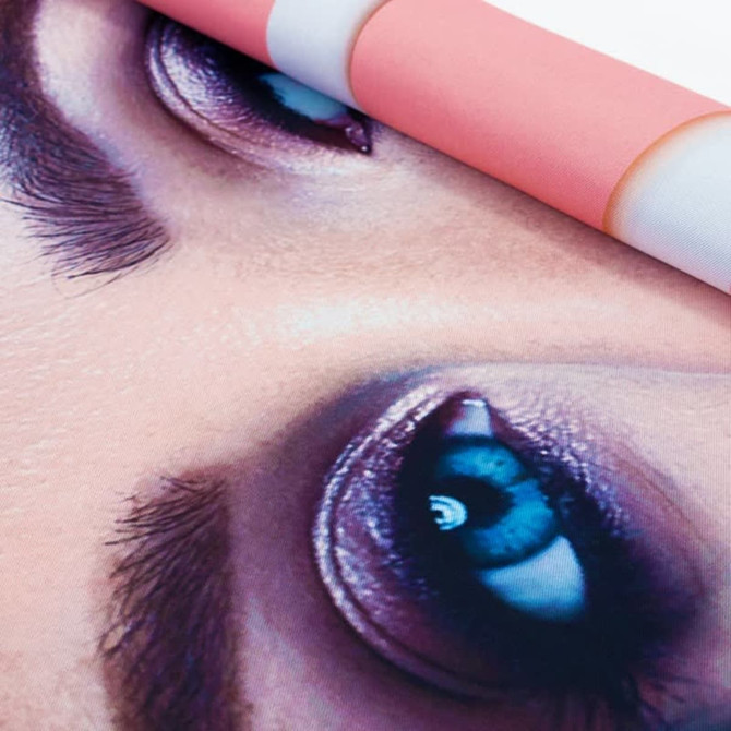 A vibrant hanging banner featuring a close-up of striking blue eyes against a pink background. It includes a logo.