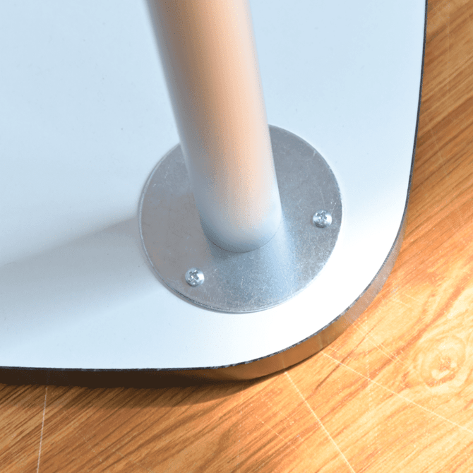 A silver metal base with a pole attached, set on a light wooden floor surface.