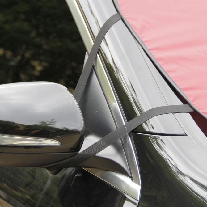 A red car shade secured with black straps, positioned against the side mirror of a vehicle.